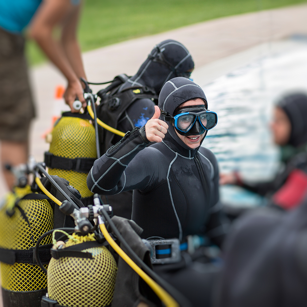 Cheerful diver with equipment sitting on pool edge and gesturing thumb up.